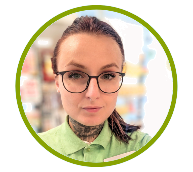 Junge Frau mit Brille, kurzen braunen Haaren und Tätowierungen, trägt ein grünes Hemd.