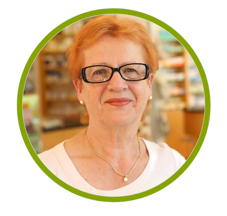 Porträt einer lächelnden Frau mit roten Haaren und Brille, in einem hellen Geschäft.