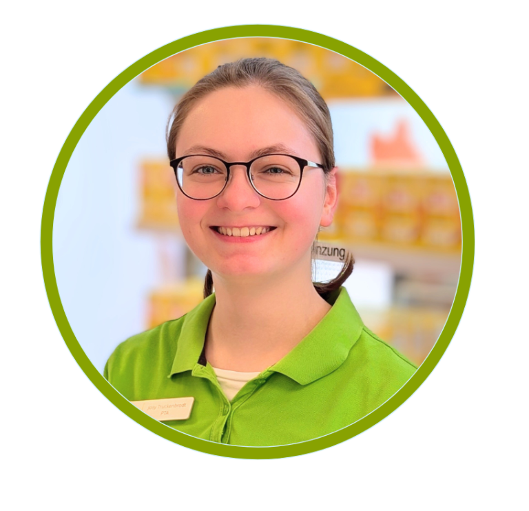 Junge Frau mit Brille und grüner Arbeitskleidung lächelt freundlich.